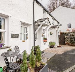Front exterior of a white cottage with small table and chairs near the door at Buttonhole Cottage in Ambleside