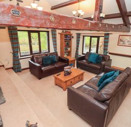 A living room with brown leather sofas a wooden coffee table a bookshelf and windows with blue striped curtains at Old Coach House Ambleside