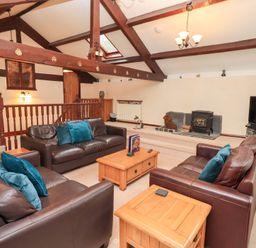 A living room with brown leather sofas and wooden tables under exposed wooden beams at Old Coach House Ambleside