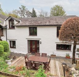 A white stone house with a wooden patio table and chairs in the garden at Old Coach House Ambleside