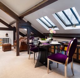 A dining area with a glass table and purple chairs under skylight windows in a room with exposed beams at Hayloft in Windermere