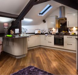 A kitchen with white cabinets wooden floor and skylight at Hayloft in Windermere