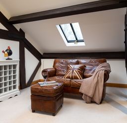A living area with a brown leather sofa and matching ottoman under a skylight at Hayloft in Windermere