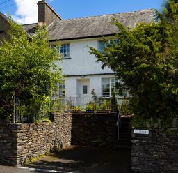 A white two story house with a stone wall and greenery at Uldale in Ambleside
