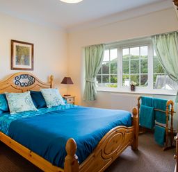 A bedroom with a wooden bed and blue bedding a window with curtains and a wooden towel rack at Uldale in Ambleside