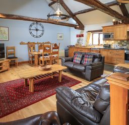 An open plan living room and kitchen with wooden furniture leather sofas and a red rug at Tullythwaite Garth in Crosthwaite