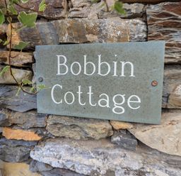 A stone wall with a metal sign that reads Bobbin Cottage at Bobbin Cottage in Ings