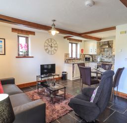 A living room with sofa red cushions armchair and dining table with kitchen in the background at Bobbin Cottage in Ings