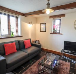 A living room with a black sofa with red cushions a glass coffee table a television and a wall clock at Bobbin Cottage in Ings