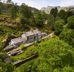 A stone house with a garden surrounded by trees and hills at The Stable At Oakbank in Elterwater
