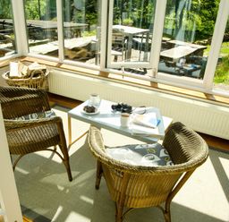 A sunroom with wicker chairs a table with coffee mugs books and binoculars at The Stable At Oakbank in Elterwater