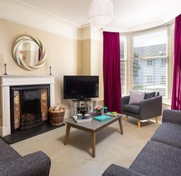 A living room with a fireplace a television a coffee table two sofas and an armchair with red curtains at Highbank in Bowness