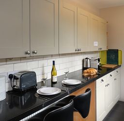 A kitchen countertop with toaster bread box wine bottle plates and chairs at Highbank in Bowness