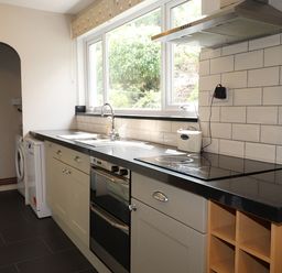 A kitchen with a black countertop oven stove sink washing machine and tiled backsplash at Highbank in Bowness
