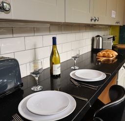 A kitchen countertop with two place settings wine bottle wine glasses toaster kettle and bread at Highbank in Bowness