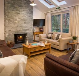 A living room with two brown sofas a beige sofa a wooden coffee table and a stone fireplace at Lanterns At Grasmere in Grasmere