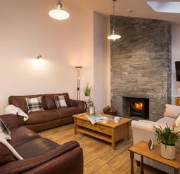 A living room with leather sofas wooden coffee tables a stone fireplace and a wall-mounted television at Lanterns At Grasmere in Grasmere