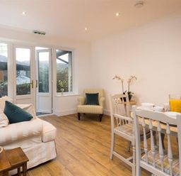 A living area with a white sofa, armchair, wooden dining table set, and glass doors at Lanterns At Grasmere in Grasmere
