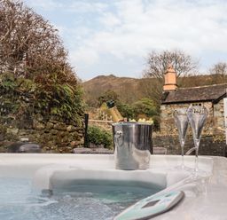 A hot tub with a champagne bottle in an ice bucket and two glasses outside a stone cottage at Hart Head Barn in Rydal