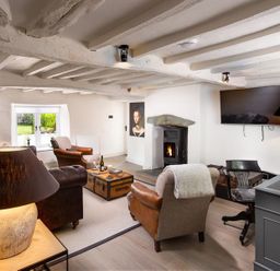 A living room with a fireplace a television a desk with a chair and leather armchairs at Underhowe in Grasmere