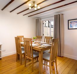 A dining room with a wooden table set for six people near glass doors at Hill Cottage Ambleside
