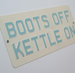 A sign on a wall that reads boots off kettle on