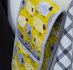 A close-up of a quilted oven mitt with sheep pattern hanging between a black cloth and a white and black checkered cloth at Hill Cottage in Ambleside