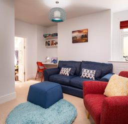A living room with a blue sofa and matching ottoman a red armchair a small desk with a red chair and shelves a window with red blinds and a landscape painting on the wall at Ellerthwaite House in Windermere