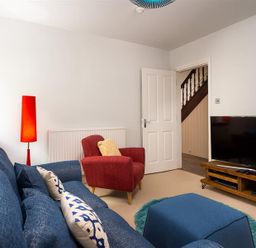 A living room with a blue sofa and ottoman a red armchair a red floor lamp and a television on a wooden stand at Ellerthwaite House in Windermere