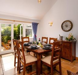 A dining room with wooden table and chairs set for a meal next to glass doors leading to a garden at Ellerthwaite House in Windermere