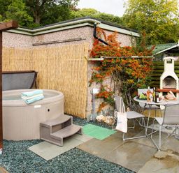 An outdoor patio area with a hot tub towels table with chairs bottles and bread near a barbecue at Heathfield in Keswick