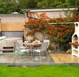 An outdoor patio with a round table and four chairs a hot tub with towels and a chimney barbecue at Heathfield in Keswick