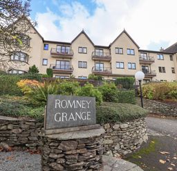 An exterior view of a multi-story residential building with balconies and a stone sign reading Romney Grange in front