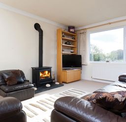 A living room with leather sofas a wood burning stove a television on a wooden stand and a large window at Honister Cottage in Ambleside