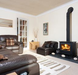 A living room with brown leather sofas a wood burning stove and a striped rug at Honister Cottage in Ambleside