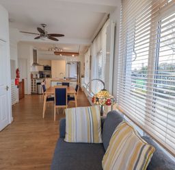 An open living and kitchen area with a dining table and chairs a ceiling fan and large windows with blinds at Windows Ambleside