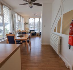 A dining area with wooden table and chairs next to large windows and a seating area with armchairs at Windows Ambleside