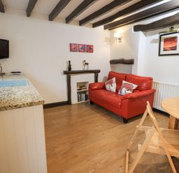 A small living room with a red sofa and wooden folding chair next to a round table and a wall-mounted TV at Cobblestone Cottage in Ambleside