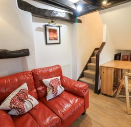 A red leather sofa with two tree patterned pillows near a small wooden dining table and staircase at Cobblestone Cottage in Ambleside
