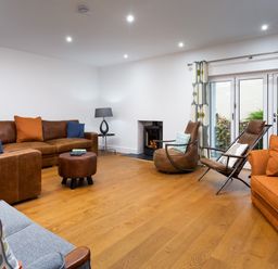 A living room with brown leather sofas orange pillows blue pillows a gray armchair a round ottoman a fireplace and glass doors with patterned curtains at Wynford in Ambleside
