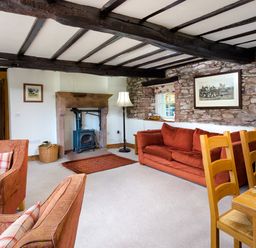 A living room with armchairs a sofa a wood burning stove wooden dining chairs and a table at Horrockwood Farm in Watermillock