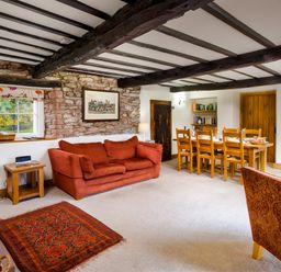 A living room with a red sofa wooden dining table with chairs and exposed wooden beams at Horrockwood Farm in Watermillock