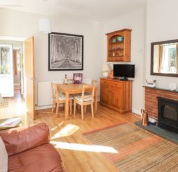 A living room with a brown leather sofa wooden dining table wooden cabinet and a brick fireplace at Courtyard Cottage Ambleside