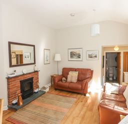 A living room with two brown leather sofas a brick fireplace with a mirror above and a view into a bathroom at Courtyard Cottage in Ambleside