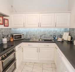 A kitchen with white cabinets grey tiled backsplash black countertops a double oven microwave sink and various kitchen utensils at Courtyard Cottage in Ambleside