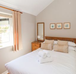 A bedroom with a double bed white bedding beige pillows wooden bedside tables and mirrors at Courtyard Cottage in Ambleside