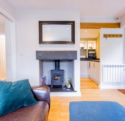 A living room with a brown leather sofa with teal pillows a wood burning stove under a mirror and a blue ottoman at Barn End in Ambleside