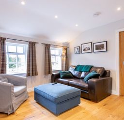 A living room with a brown leather sofa green cushions blue ottoman gray armchair and three framed pictures on the wall at Barn End in Ambleside
