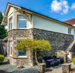 An exterior view of a two story stone and plaster house with outdoor seating and stairs at Skyfall in Bowness