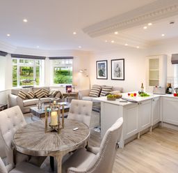 An open plan kitchen and living room with a round dining table four chairs two sofas and white kitchen cabinets at Skyfall in Bowness